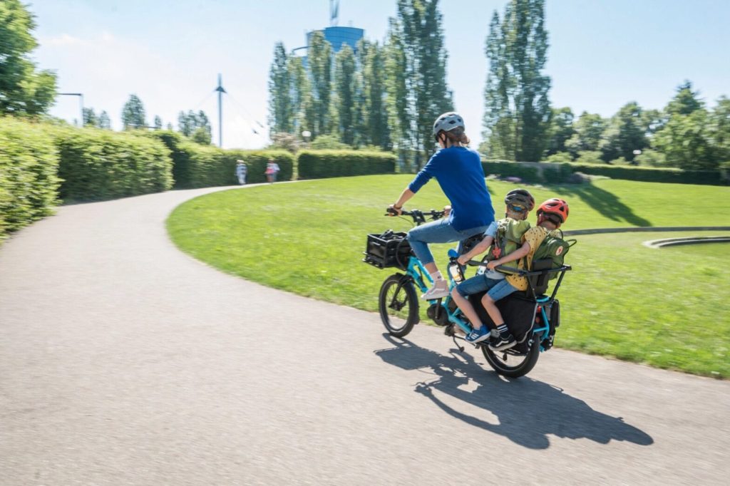 parent riding a trike = with 2 kids on seat behind